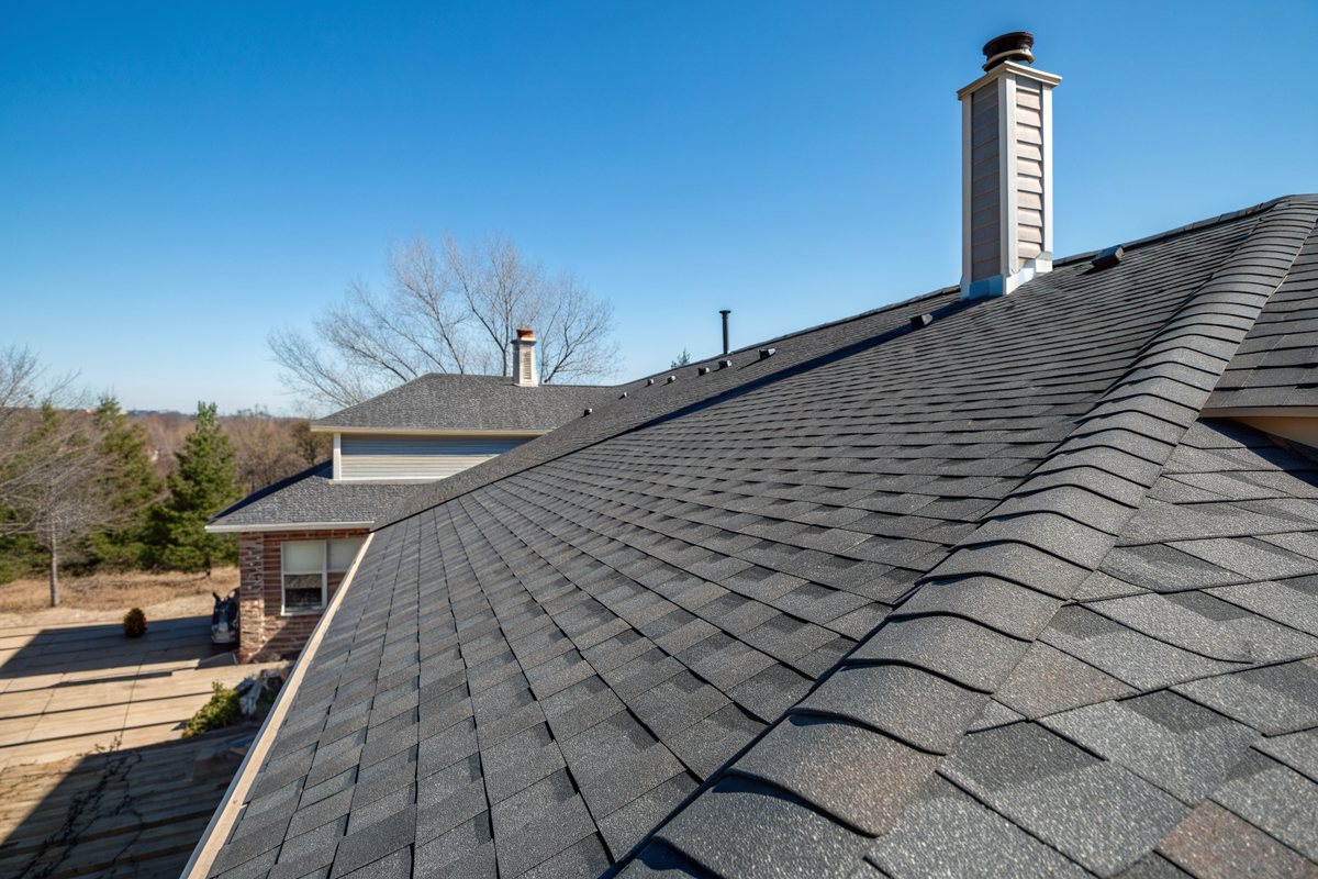 A ridge vent along the peak of a new dark shingle roof under a blue sky